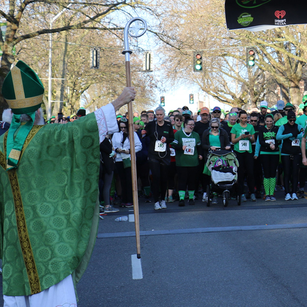 A man wearing a green robe stands in front of a starting line full of runners.