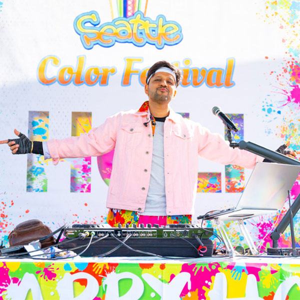 DJ with arms out in front of a backdrop titled, Seattle Color Festival.