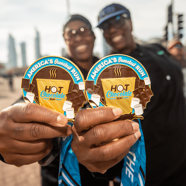 Two people proudly display hot chocolate shaped medals, smiling at the camera.