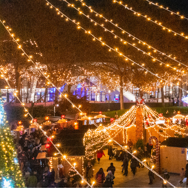 Busy outdoor nighttime Christmas market filled with lights.