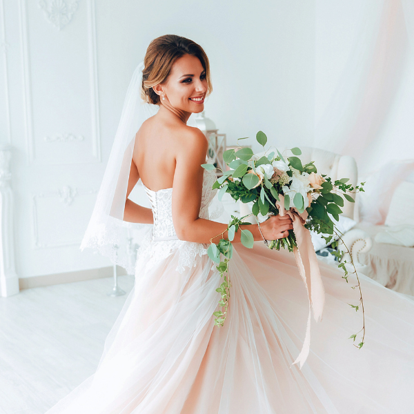 Happy woman in a wedding dress holding a bouquet in a white room.