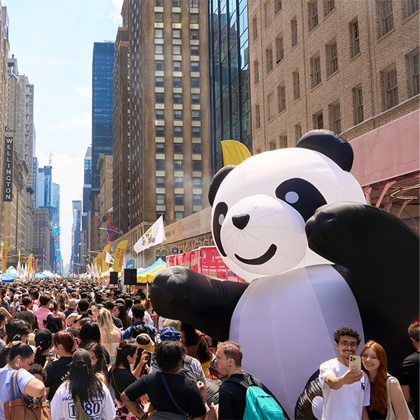 Crowded food festival on a city street featuring a large inflatable panda.
