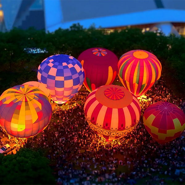 Nighttime aerial view of an outdoor lawn filled with colorful glowing hot air balloons.