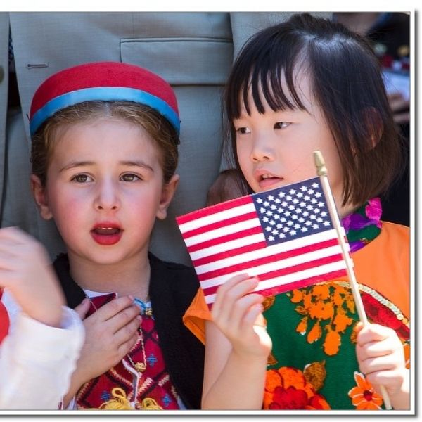 Girls dressed in traditional clothing and waving an American flag