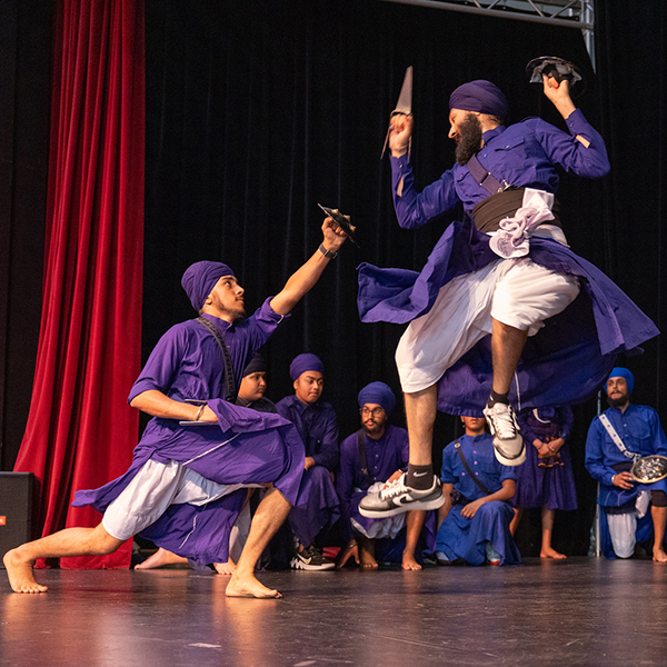 Men in purple turbans and robes performing martial arts on stage.