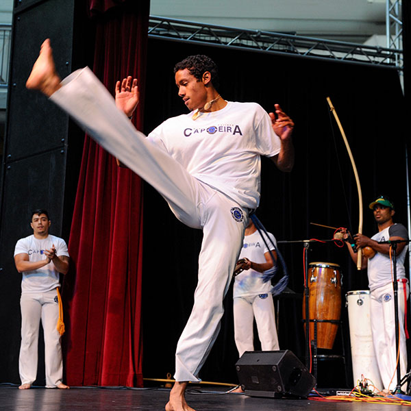 Man in a white martial arts outfit performing a high kick on stage.