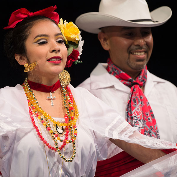 A smiling woman and man in white outfits and colorful, festive accessories.