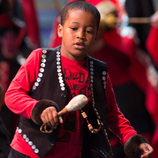 Child performers in red shirts and black vests playing instruments.