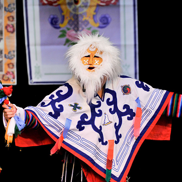 Masked performer in a traditional Tibetan outfit with arms raised.