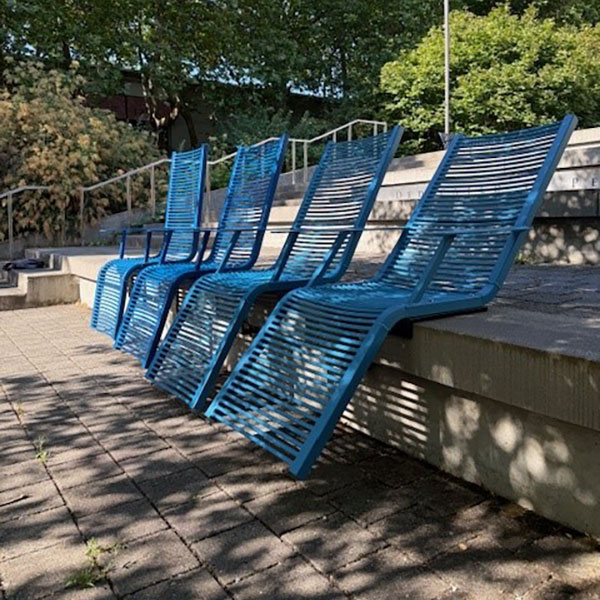 Four blue metal reclining chairs are installed in an outdoor plaza.
